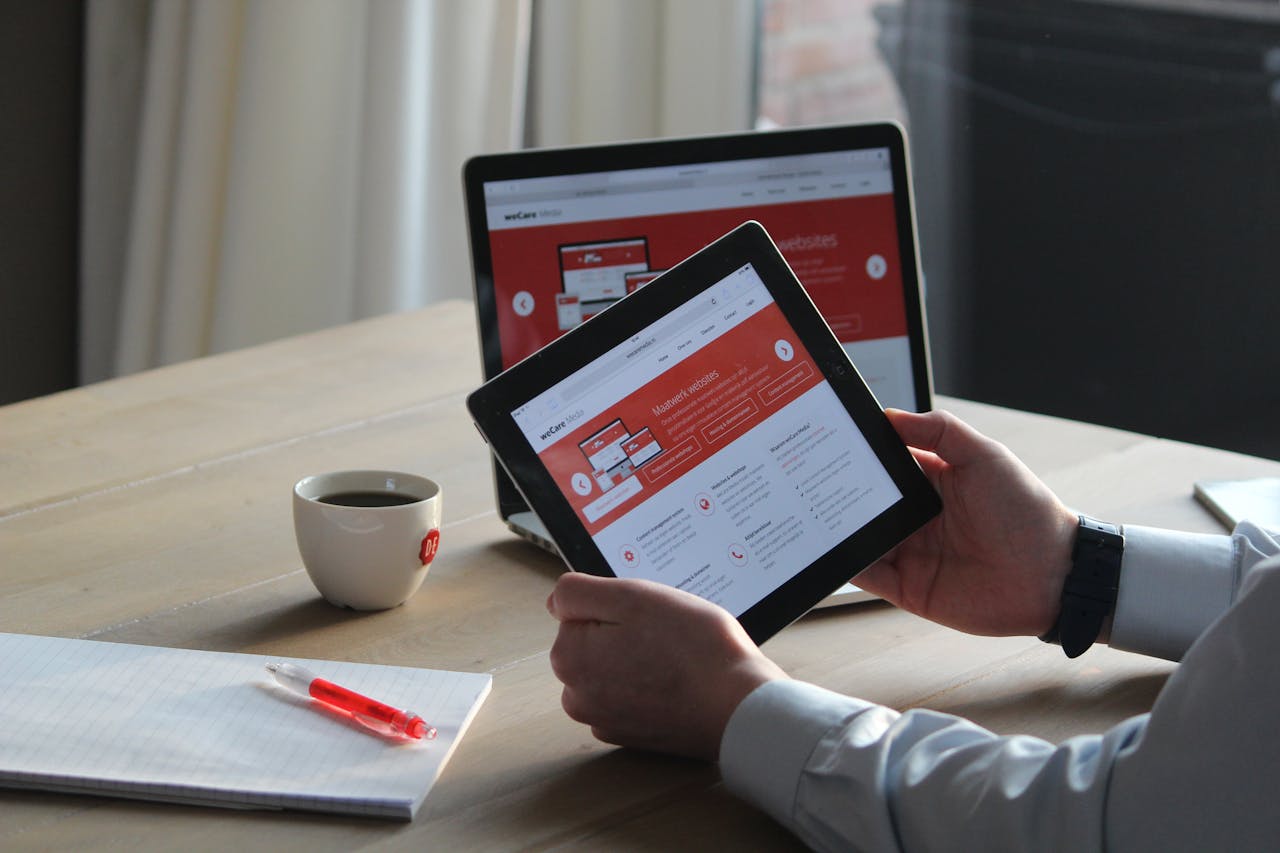 services-03 Business professional using a tablet and laptop with a hot drink, focusing on digital content review.